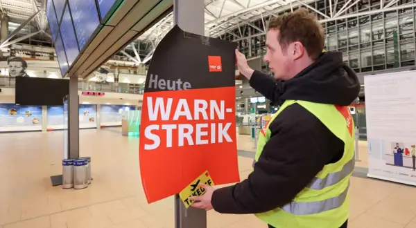 Ein Mann mit Warnweste befestigt ein Schild "Heute WARN-STREIK" an einem Pfosten. Hier wird heute gestreikt.