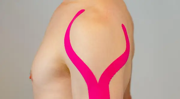 Schulter tapen: Ein Mann mit pinkem Kinesio-Tape auf der Schulter, das wie ein aufgeschlagenes Buch aussieht.