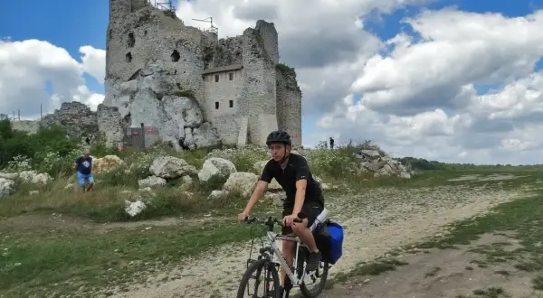 Młody mężczyzna na rowerze przemierza malowniczą trasę po Jurze Krakowsko-Częstochowskiej, mijając ruiny zamku.
