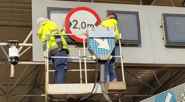 Pracownicy na podnośniku montują znak ograniczenia wysokości 2,0m przy bramkach viatoll.