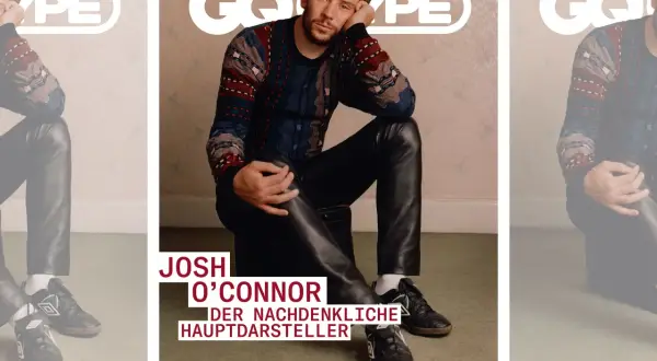 Josh O'Connor, der nachdenkliche Hauptdarsteller, sitzt lässig in Lederhosen und einem gemusterten Pullover.