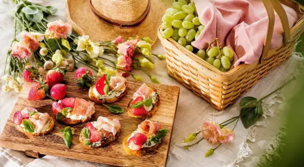 En härlig picknick med bruschetta, jordgubbar, vindruvor i korg och en stråhatt. Perfekt picknick mat för en solig dag.