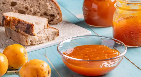 Pane rustico, nespole fresche e una ciotola colma di deliziosa marmellata di nespole, pronta per essere gustata.