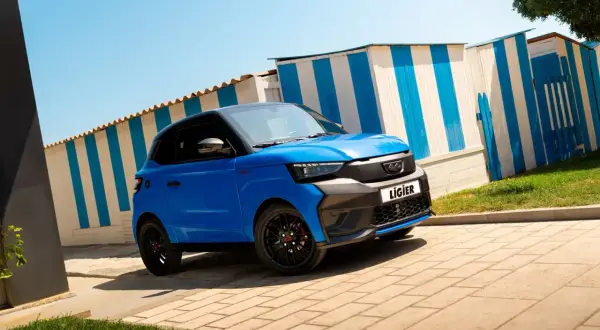 Voiturette bleue Ligier garée devant des cabines de plage rayées. Idéale pour la nouvelle loi voiture sans permis.