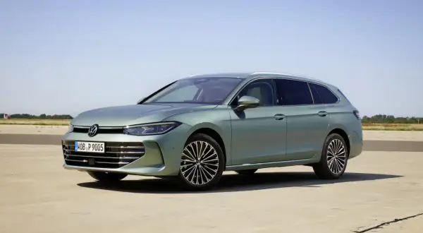 Nowy Volkswagen Passat B9 w kolorze zielonym, zaparkowany na betonowej nawierzchni, z błękitnym niebem w tle.