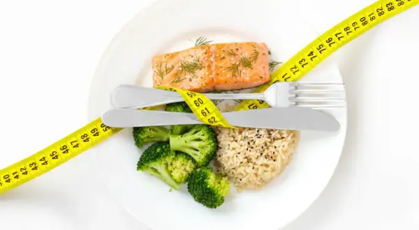 Gesundes Essen für schnelles Abnehmen: Lachs, Brokkoli und Reis, umgeben von einem Maßband.