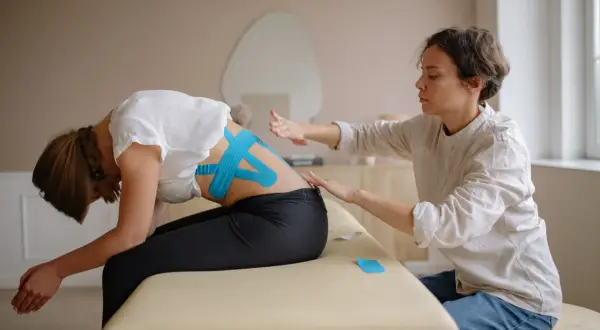 Fizjoterapeutka z taśmami kinezjotaping na plecach pacjentki. Zastanawiasz się, ile zarabia fizjoterapeuta w Norwegii?