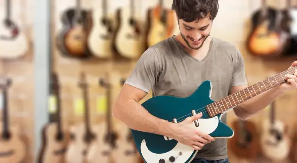 Młody mężczyzna wybiera **jaką gitarę elektryczną na początek** w sklepie muzycznym.