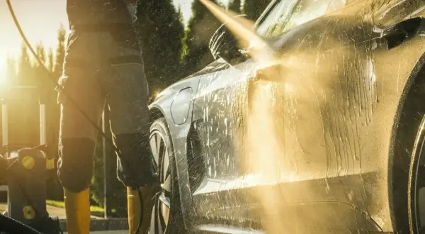 Słońce zachodzi, a Ty uczysz się, jak myć auto na myjni ciśnieniowej. Woda spływa po lśniącej karoserii.