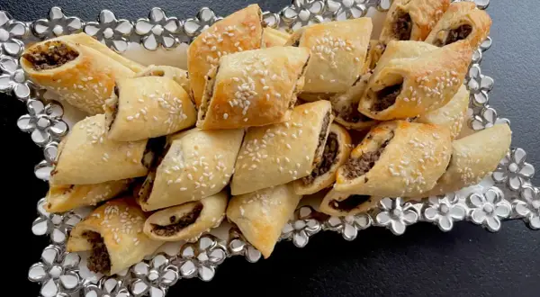 Paszteciki z pieczarkami i serem, posypane sezamem, ułożone na ozdobnej tacy z kwiatowymi zdobieniami.