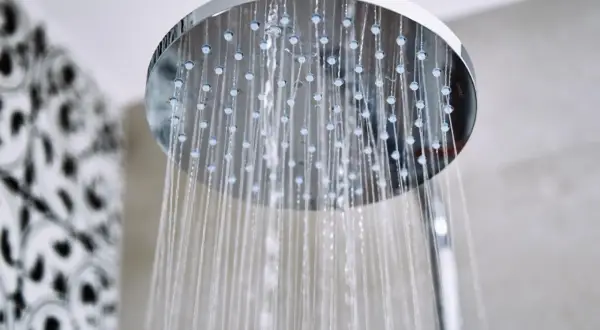 Acqua che scorre da un soffione doccia moderno, un promemoria per sapere come pulire il soffione della doccia per un getto perfetto.