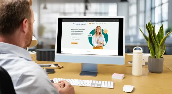 Mężczyzna pracuje przy komputerze, na ekranie którego widoczna jest strona internetowa z rankingiem agentów ubezpieczeniowych.