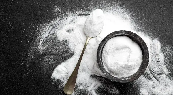 Un cucchiaio e una ciotola pieni di carbonato di sodio, mostrando i suoi molteplici usi in cucina e per la pulizia.