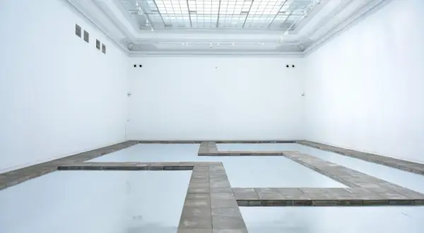 Biała przestrzeń galerii z lustrzaną podłogą i kamiennymi ścieżkami tworzącymi labirynt. Kojący widok, jakbyś spacerował po chmurach.