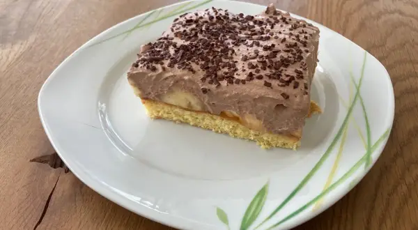 Ein Stück Bananen Torte mit Schokoladencreme und Schokostreuseln auf einem Teller mit Blattmuster.