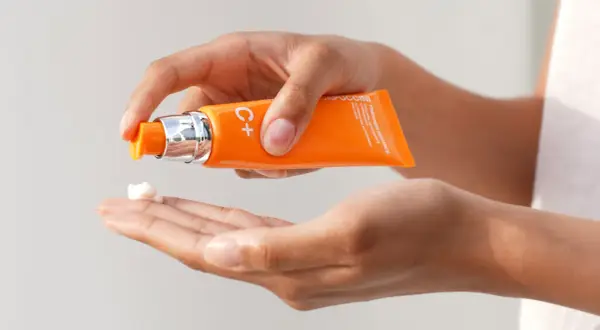 Mani che dosano una crema con vitamina C sulla pelle, per un trattamento illuminante e antiossidante.