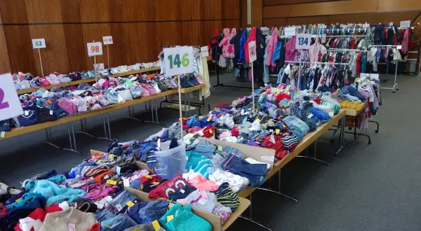 Großer kinderflohmarkt in Bergisch Gladbach mit Kleidung auf Tischen und Kleiderstangen.