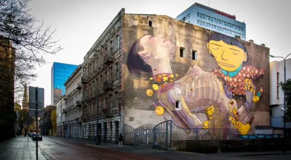 Imponujące street art na ścianie kamienicy, przedstawiające surrealistyczną scenę z postaciami i elementami anatomicznymi.