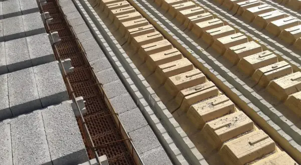 Budowa stropu: betonowe pustaki i zbrojenie w rowkach, obok żółte pustaki szalunkowe. Określanie grubości stropu.