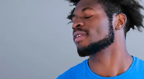 Un homme avec une barbe collier épaisse, les yeux fermés, porte un t-shirt bleu vif.