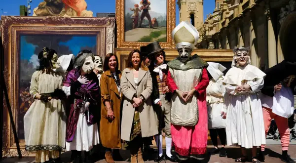 Personas enmascaradas y vestidas con trajes de época posan frente a cuadros, recreando el espíritu de las fiestas goyescas.