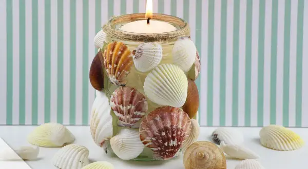 Kerzenglas mit Muscheln verziert, ein schönes Beispiel für basteln mit Muscheln. Ein warmes Licht scheint durch die maritime Dekoration.