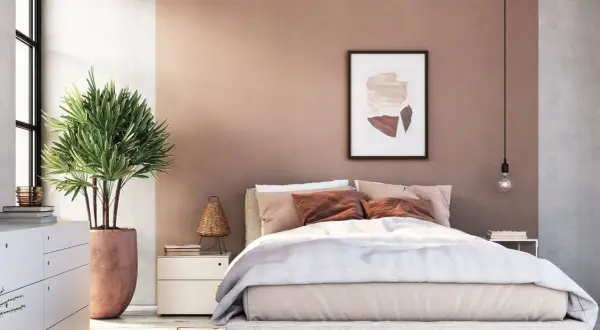 Gemütliches Schlafzimmer mit sanfter, rosafarbener Wandfarbe. Ein großes Bett mit beiger Bettwäsche und braunen Kissen lädt zum Entspannen ein.