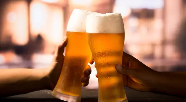 Due mani brindano con due bicchieri di birra ghiacciata, un momento di piacere che celebra la birra proprietà.