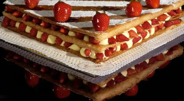 Una magnifica torta millefoglie con strati di pasta sfoglia, crema pasticcera e fragole fresche, decorata con fragole intere e zucchero a velo.