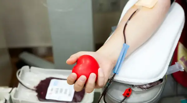 Dłoń trzymająca czerwone serce podczas oddawania krwi. Zastanawiasz się, ile dni wolnego za oddanie krwi? To ważna decyzja.