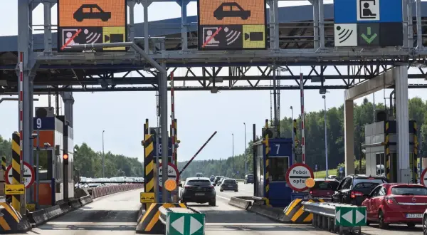 Bramki autostradowe A4 z wyświetlaczami informacyjnymi i szlabanami, w tle samochody.