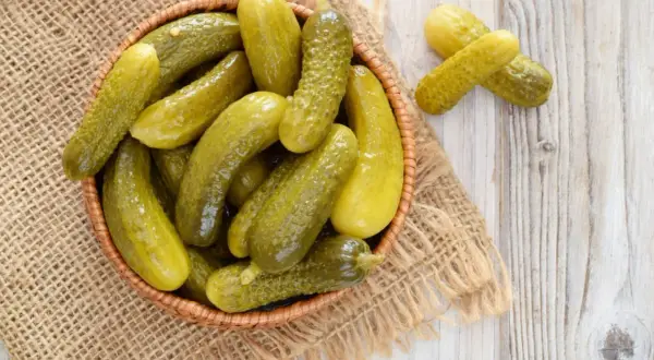 Koszyk pełen kiszonych ogórków na jutowym płótnie. Zastanawiasz się, ile kcal ma ogórek kiszony? To zdrowa przekąska!