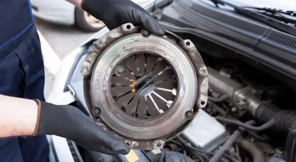 Mechanic holding a car clutch assembly with engine in background.