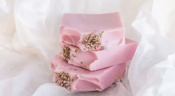 Zarte rosa Seifenstücke mit Lavendelblüten, inspiriert von Quillaja Saponaria, liegen auf weißem Papier.