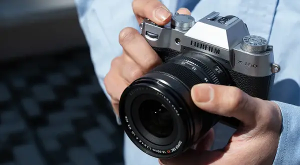 Dłonie trzymające srebrny aparat Fujifilm X-T50 z obiektywem Fujinon.