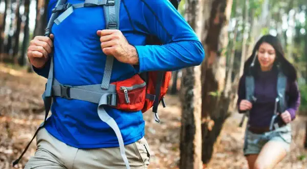 Un hombre y una mujer caminan por un sendero boscoso, ambos con una mochila mountain lista para la aventura.