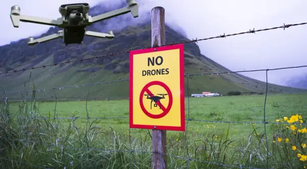 Un drone vola vicino a un cartello "Vietato l'utilizzo drone" in un paesaggio rurale nebbioso.