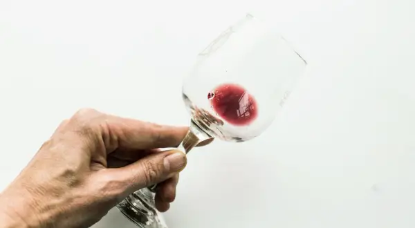 Mano che tiene un bicchiere di vino rosso, con un residuo che ricorda l'acido tartarico, essenziale per la sua conservazione.
