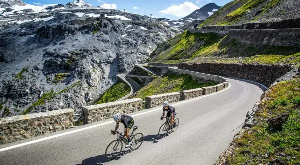 Dwóch kolarzy pokonuje serpentyny na przełęczy Stelvio, otoczeni surowym, górskim krajobrazem.