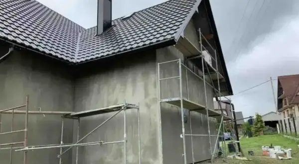 Dom w trakcie prac elewacyjnych, rusztowania wokół, szara ściana. Sprawdzamy elewacja cena za m2 robocizna.