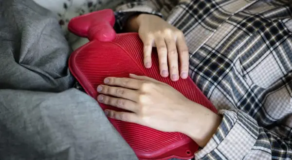 Mani che stringono una borsa dell'acqua calda rossa, un rimedio casalingo per il sollievo dal dolore, un esempio di ipertermia terapia.