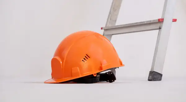 Pomarańczowy kask leży obok drabiny, gotowy do pracy.