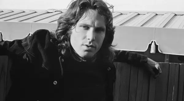 Jim Morrison, wokalista The Doors, oparty o drewniany płot, zamyślony.