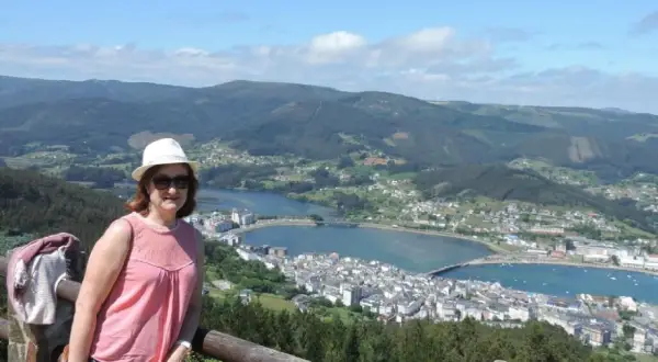 Mujer con sombrero blanco y blusa rosa posa en el mirador de San Roque, disfrutando de la vista panorámica de la ría y el pueblo.