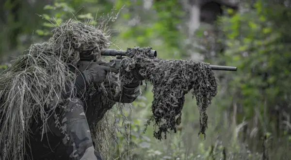 Un francotirador camuflado en un bosque, listo para la acción. El airsoft, un deporte que simula combates, requiere sigilo y estrategia.