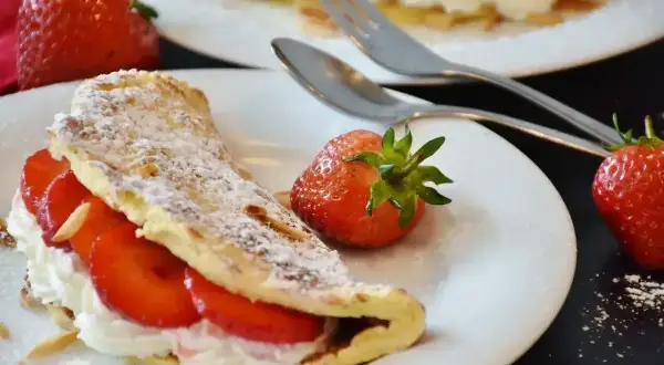Pyszny omlet z białek z bitą śmietaną i truskawkami, posypany cukrem pudrem i płatkami migdałów.