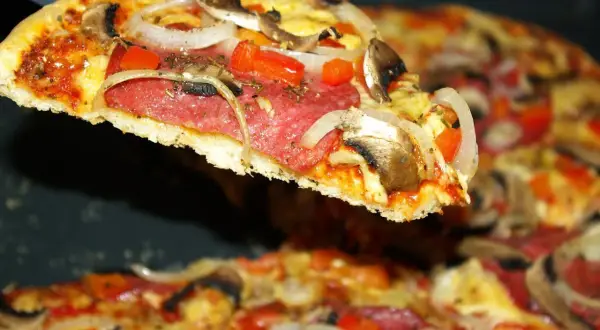 Kawałek pysznej pizzy salami z pieczarkami i cebulą, unoszący się nad resztą zapiekanki.