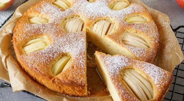 Ein goldbrauner Apfelkuchen, bestäubt mit Puderzucker, mit saftigen Apfelscheiben. Omas weltbester Apfelkuchen, ein Stück davon ist bereits angeschnitten.