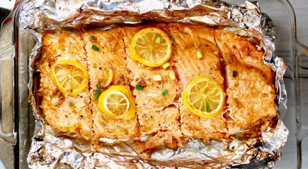 Pyszny, pieczony filet z łososia z plasterkami cytryny i szczypiorkiem, podany w folii aluminiowej.