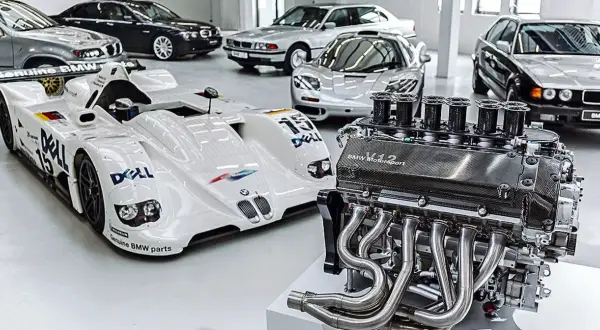 Silnik V12 BMW Motorsport obok białego bolidu wyścigowego i kilku klasycznych BMW.